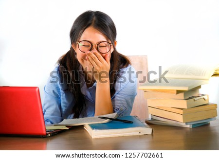young sweet and happy Asian Korean student girl in nerd glasses working cheerful on laptop computer on desk with pile of books studying and smiling isolated on white background 