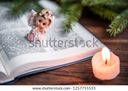 The Bible, angel and candle on wooden background with fir branches. Christian faith. Christmas Day.