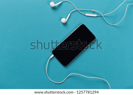 Mobile phone with white earphones on colour backgroung, top view
