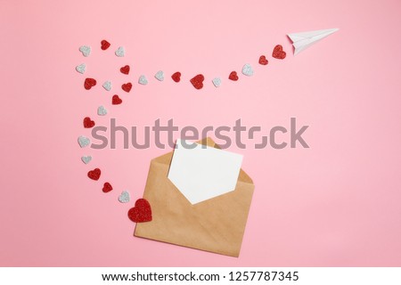 Distance love concept, sending love letter, valentines day. Kraft envelope with blank postcard and paper airplane flying on route made of heart shaped valentines cards lay on pink background desk Royalty-Free Stock Photo #1257787345