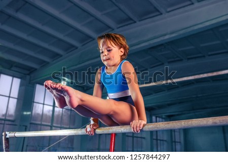 The beautiful little girl is engaged in sports gymnastics on a parallel bars at gym. The performance, sport, acrobat, acrobatic, exercise, training concept Royalty-Free Stock Photo #1257844297