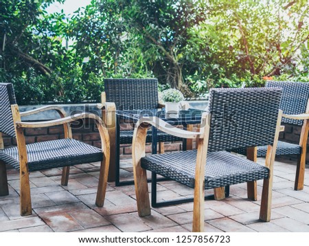 Four Outdoor wooden and woven armchairs and glass table on brick floor near the garden.