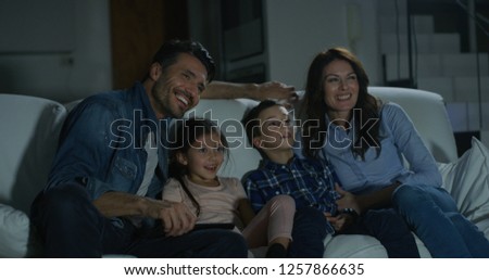 Portrait of happy family watching TV on sofa in the evening in living room. Concept of family entertainment, education, technology.