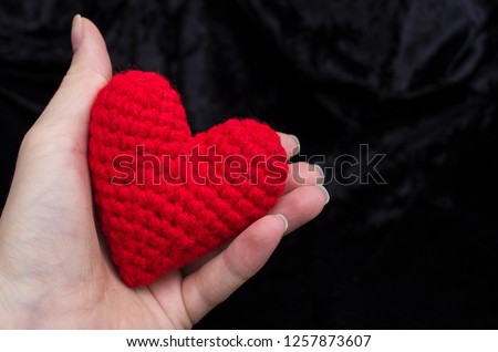 
yarn knitted red heart hold a woman in her hand. background