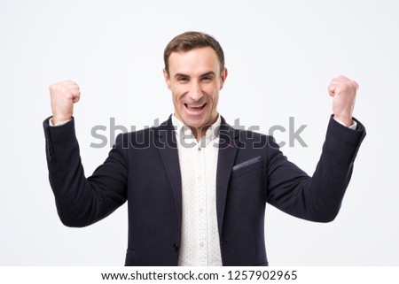 I am a winner concept. Pleased and happy young italian man is smiling broadly and showing victory sign with both hands.