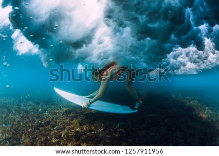 Attractive surfer woman dive under crashing barrel wave.