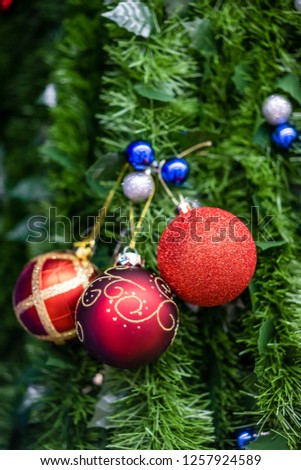 Three red and gold Christmas decoration balls hanging on a green spruce branch with smaller silver and blue balls