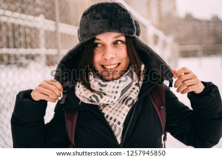 portrait of a beautiful blonde in a hat and scarf on the background of the city landscape in the cold season. girl walking down the street
