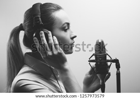 Young beautiful girl records vocals, radio, voiceover tv, reads poetry, blog, podcast in the studio on the studio microphone with headphones on a white background. Black and white photo