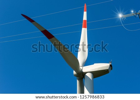 Detail a white and red wind turbine with a power line on a clear blue sky - Renewable energy concept
