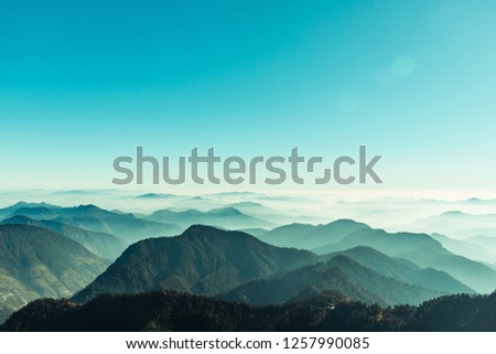 View of Himalayas mountain range with visible silhouettes through the colorful fog from Khalia top trek trail. Khalia top is at an altitude of 3500m himalayan region of Kumaon, Uttarakhand, India. Royalty-Free Stock Photo #1257990085