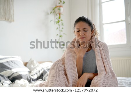 Attractive brunette sitting on bed with sore throat Royalty-Free Stock Photo #1257992872