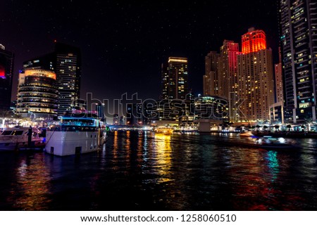 Dubai Marina at night with light reflections on the water, starry sky and a dhow cruise