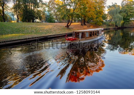 A boat with tourists is floating along the channel in the park of Riga, Latvia. Amazing reflection in the water.