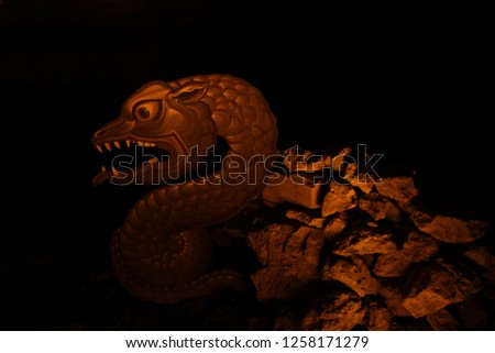 Figure of an angry snake dragon coming out from stones in a cave with low light is protecting the entrance from unwanted visitors isolated in black background
