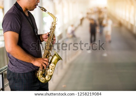 A street musician plays the saxophone with blurry people walking on skywalk in city.