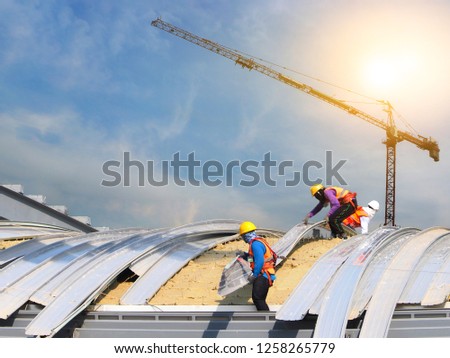 construction workers wearing safety harnesses to working on high places to roofing large building in construction site Royalty-Free Stock Photo #1258265779