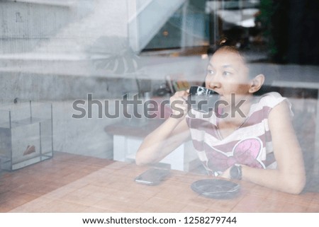 Picture through the window of young asian woman have leisure time to drink hot coffee in the coffee shop. 
