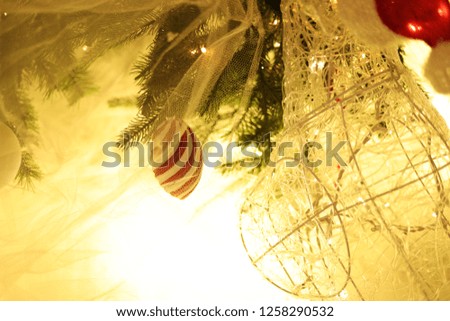 A small red and white spiral ornament on a christmas tree against a background of bright yellow light, with lace fabric in the foreground.