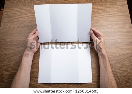 Mens hands holding empty white booklet on wooden background. View from above
