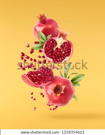 Flying in air fresh ripe whole and cut pomegranate with seeds and leaves isolated on yellow background. High resolution image Royalty-Free Stock Photo #1258354621