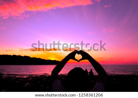 Silhouette of made heart shape and a young romantic couple on background colorful sunset on the sea beach, Love concept
