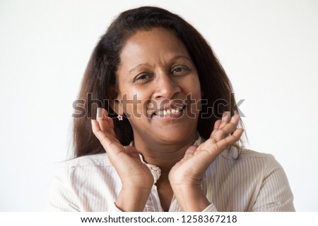 Closeup of happy Latin woman with hands at face. Mid adult lady smiling at camera. Positive emotion concept