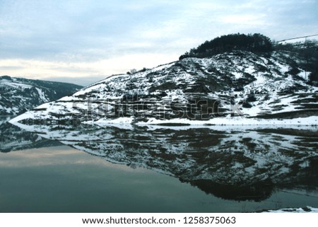 landscape of snowy mountains reflecting in the still lake water with mist creeping in, serene idyllic vista - Image