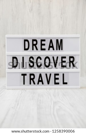 Modern board with text 'Dream Discover Travel' word over white wooden surface, side view. Closeup.