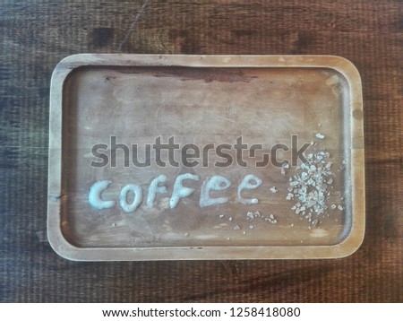 Crystalline sugar on old wooden tray with traces of coffee mug. And a milk froth. Write the word coffee as a symbol of a drink containing caffeine.