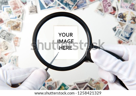 Hands in white gloves holding postage stamp copy space with a forceps and magnifier above the stamps on the table