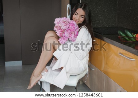 a young girl in a white robe holding a bouquet of peonies in the kitchen brown