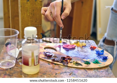 cropped image of left-handed artist taking paint from palette in workshop