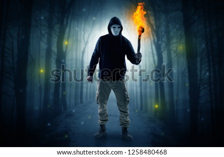 Mysterious man coming from a path in the forest with burning flambeau concept