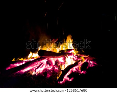 Campfire in pitch black night. Perfect for roasting marshmallows on a cozy night. Pictured is a campfire burning bright orange and angry red to warm the surroundings. 