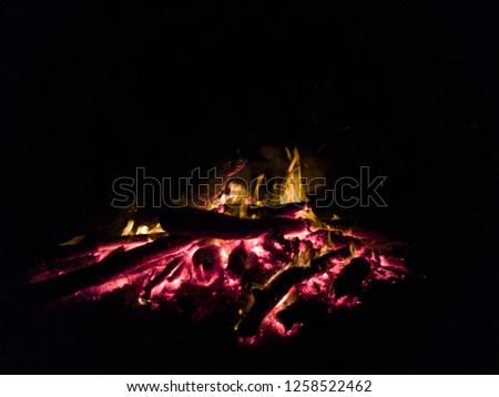 Slow burning camp fire, with amber colored logs. campfire, in the pitch black night perfect for long conversations and marshmallows. 