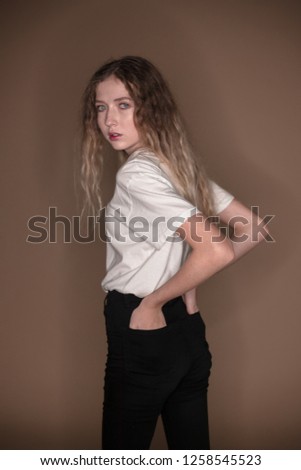 The portrait of a young girl with blonde hair isolated on a brown background wearing white t-shirt thinking concerning looking camera posing
