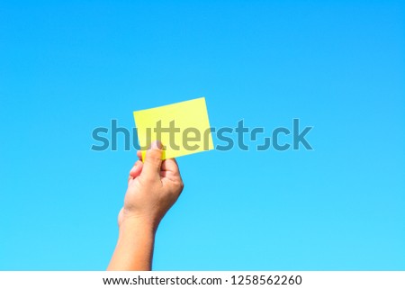 A male hand holds a green paper card with the blue sea as a background.
