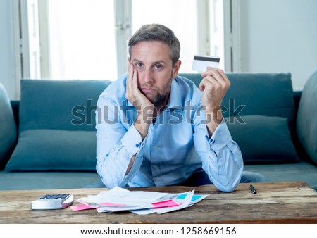 Desperate entrepreneur young man in credit card debt calculating bills tax expenses and counting business or home finances sitting on couch in paying off debts banking and financial problems concept.