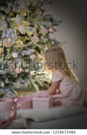 Girl with blond hair in pink dress near the elegant new year tree. Merry Christms time,