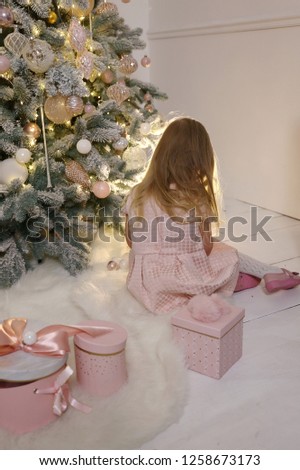 Girl with blond hair in pink dress near the elegant new year tree. Merry Christms time,