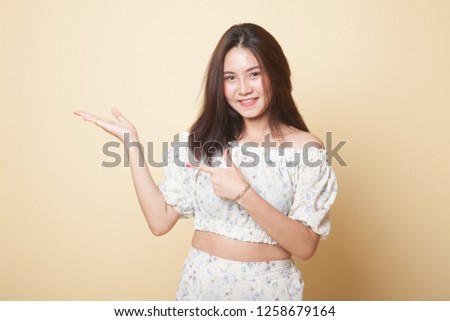Beautiful young Asian woman point to palm hand on beige background