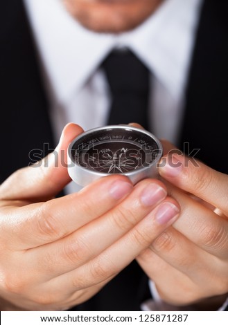 Businessman looking at a compass which he is holding in his hand with focus to the compass