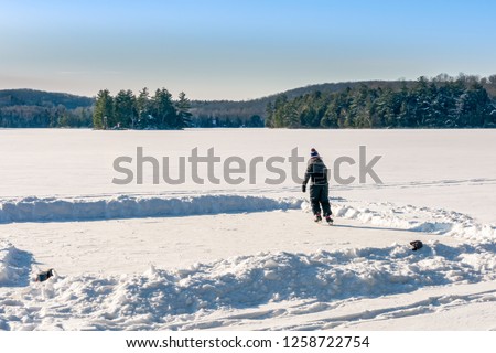 Unidentifiable boy, dressed in snow gear as he skates on a portion of a vast frozen lake, which has been cleared of snow to create a natural skating rink. concept, copyspace, background.