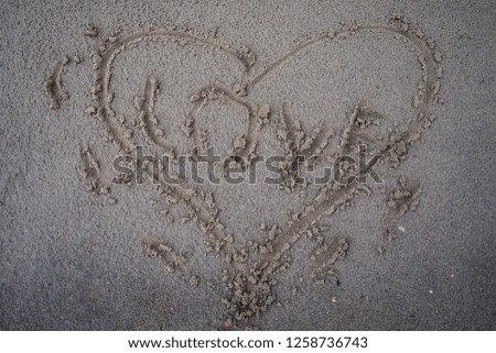 Heart is drawn in the sand of a beach by a stick in the center of the inscription love.