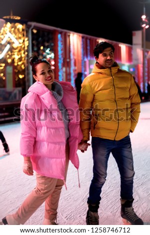 Young family skating in the ice rank dressed in pink and yellow  jacket  at night and the garland is shining 