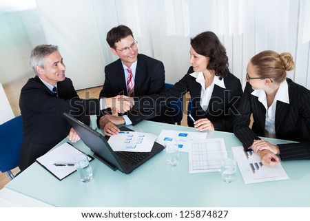 Business colleagues seated around a table in a meeting congratulating one another by shaking hands Royalty-Free Stock Photo #125874827