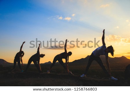 Silhouette of young womans practicing yoga or pilates at sunset or sunrise in beautiful mountain location