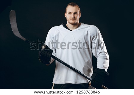 Handsome caucasian hockey player posing with gaming stick at studio, looking at camera with confident look, isolated over black background. Smiling at camera isolated, over black background
