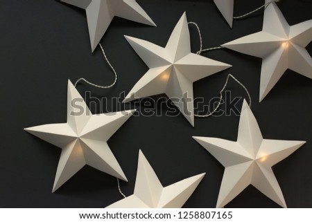 White paper stars on dark background. Electric christmas garland. Sweden design